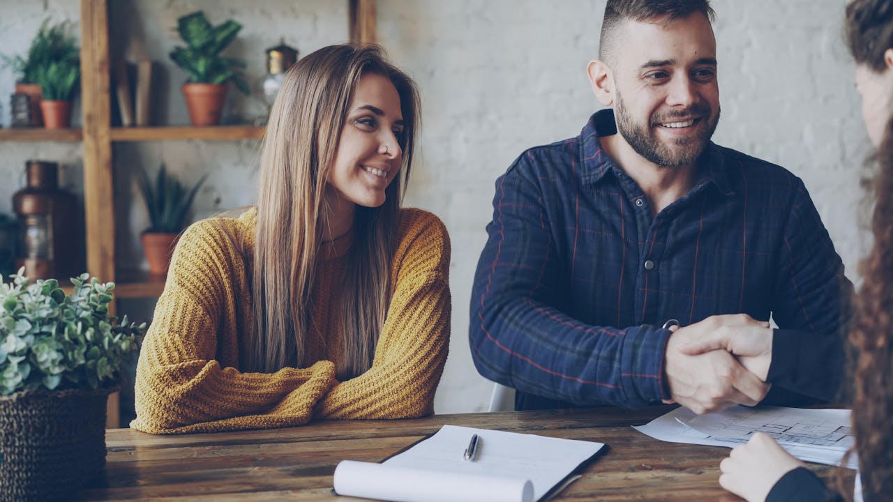 Couple securing a deal with handshake, smiling in a casual setting.
