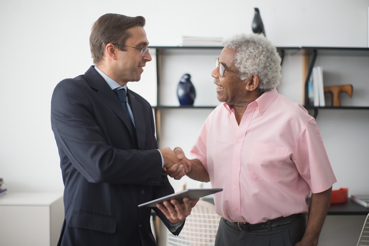 Two businessmen shaking hands during a meeting in a bright office environment.